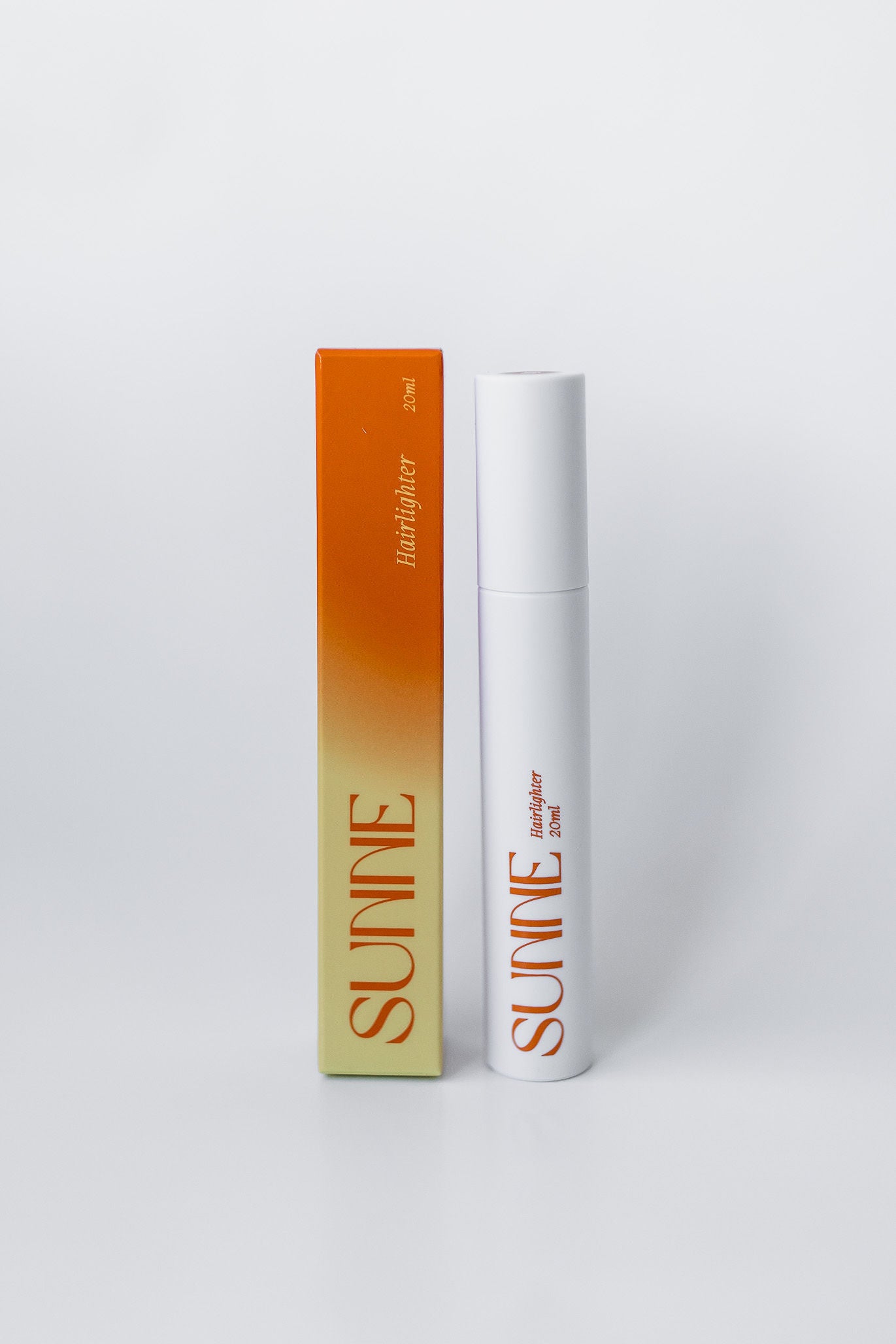The Sunne Hairlighter product and packaging displayed on a white background, highlighting the sleek white tube and gradient orange box design.